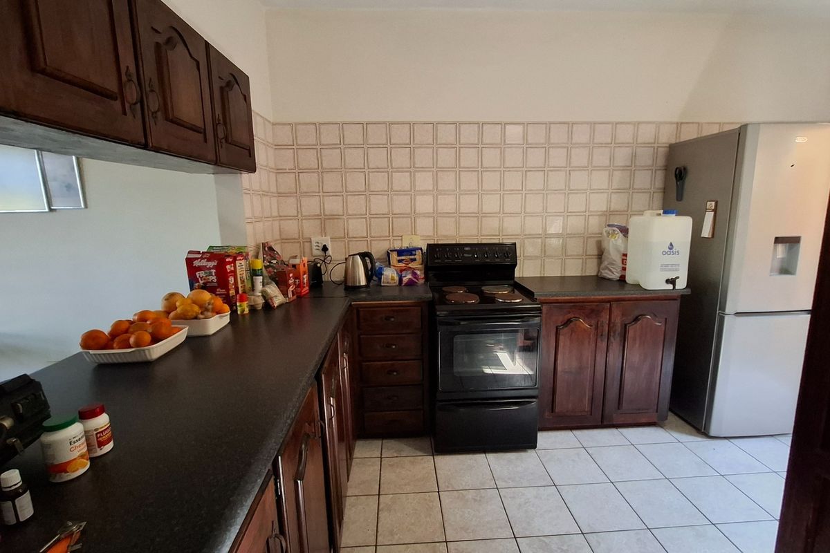 A functional kitchen featuring dark wood cabinetry, laminate countertops, a tiled backsplash, and a freestanding electric stove with ceramic floor tiles.
