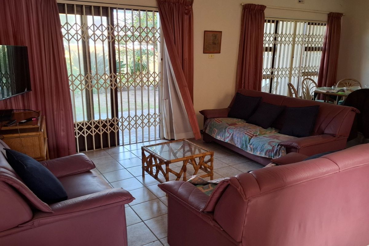 A spacious living room featuring tiled flooring and large sliding glass doors with security gates, providing direct access to the outdoor area.