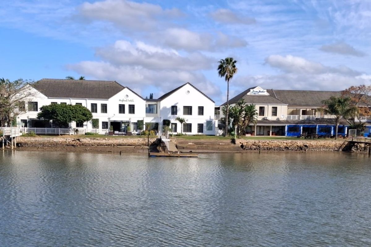 A scenic waterfront view of a commercial property complex featuring white multi-story buildings, pitched roofs, and direct access to the water via a jetty.