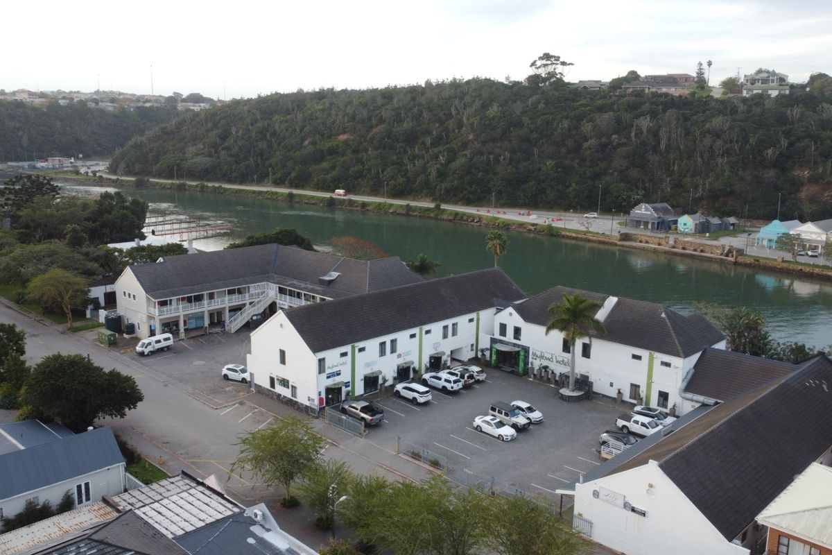 Aerial view of a commercial property complex featuring multiple buildings, a paved parking area, and proximity to a river and natural landscape.