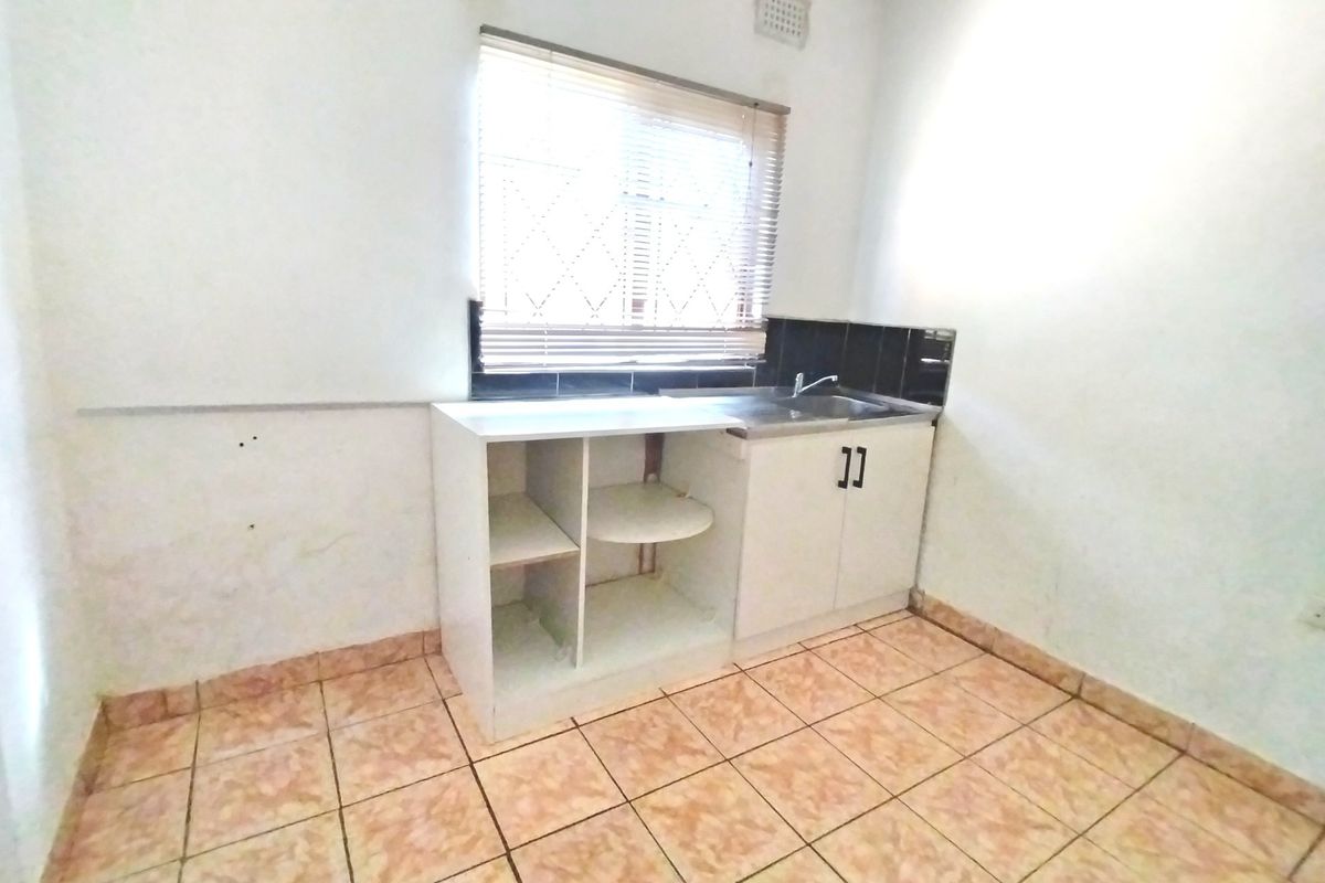 A compact kitchen area featuring tiled flooring, a single sink, and basic built-in cabinetry with open shelving.
