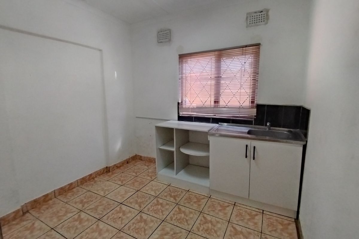 A compact, empty kitchen area featuring tiled flooring, a stainless steel sink, and basic built-in cabinetry with a tiled splashback.