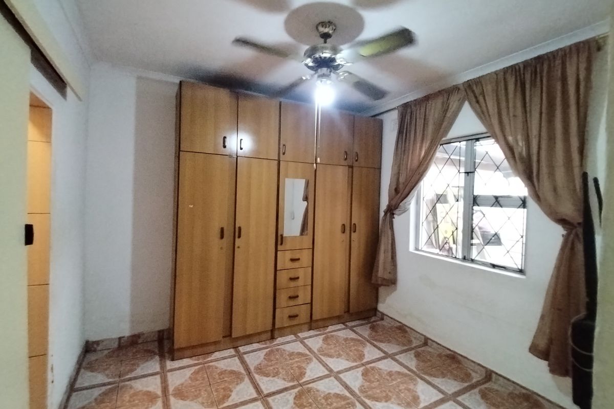 A bedroom featuring built-in wooden cupboards, tiled flooring, and a ceiling fan, offering a functional space with potential for modern updates.