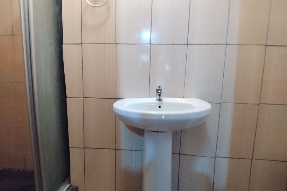 A functional bathroom featuring a white pedestal basin with a chrome mixer tap and full-height wall tiling.