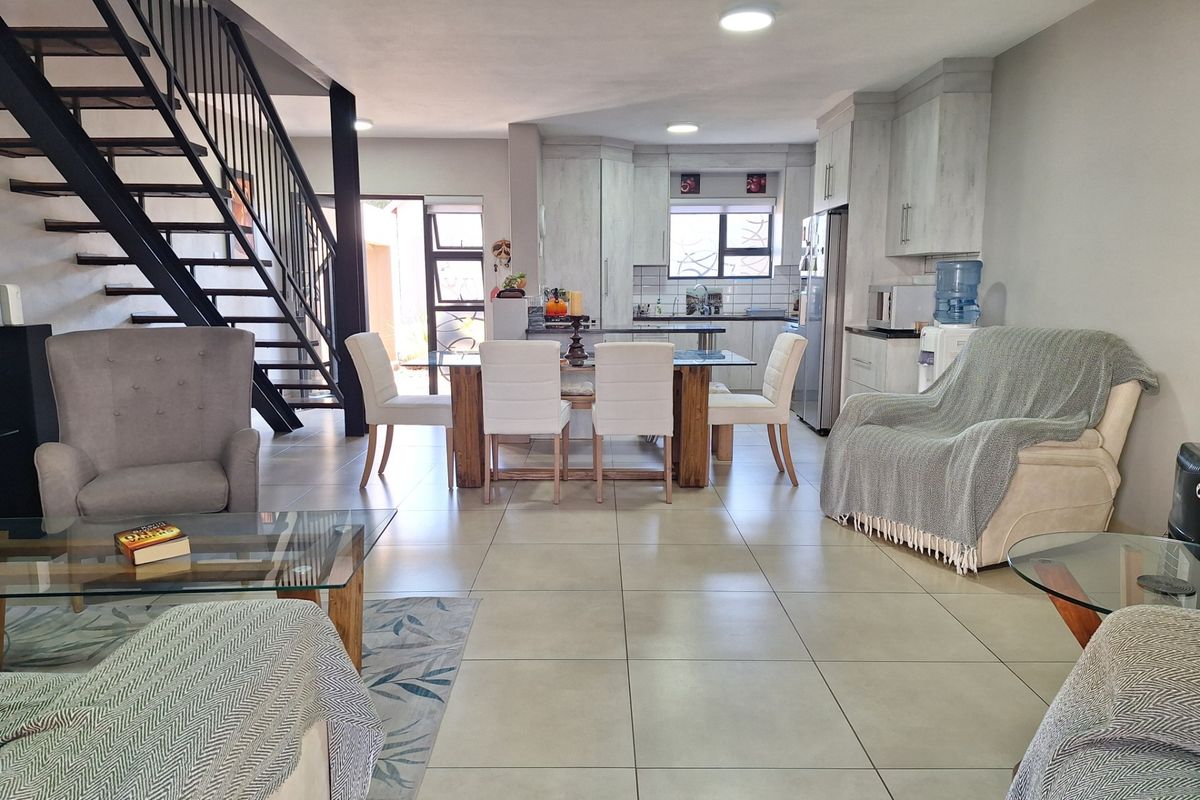 Spacious open-plan living and kitchen area featuring modern tiled flooring, a striking metal staircase, and functional built-in cabinetry.