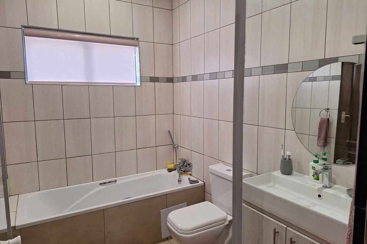 A well-maintained bathroom featuring a bathtub, toilet, and a vanity unit with a basin, finished with neutral wall and floor tiling.