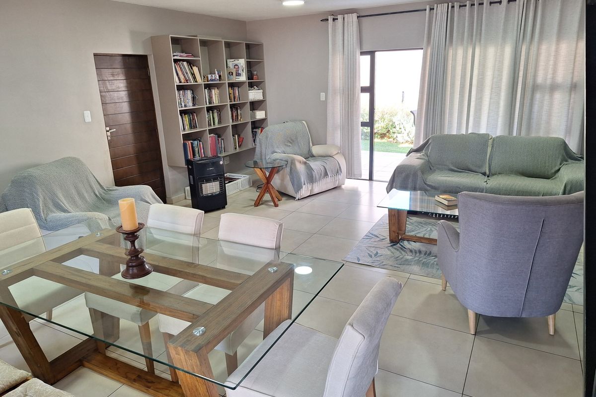 Spacious open-plan living and dining area featuring neutral tiled flooring, built-in shelving, and direct access to the outdoor patio through sliding glass doors.