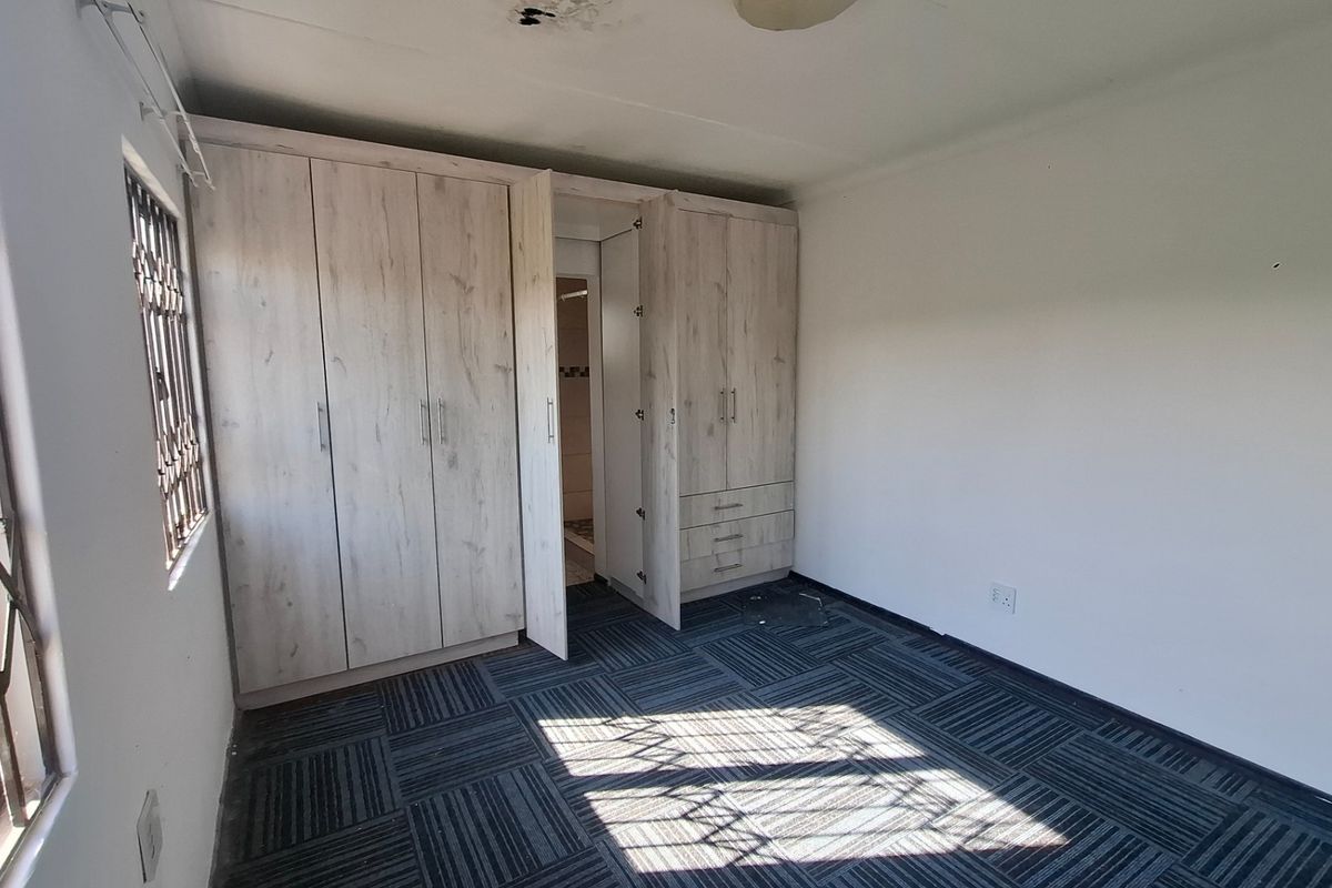 A bedroom featuring built-in cupboards, carpet tile flooring, and security bars on the window. The room requires ceiling repairs and a new light fixture.