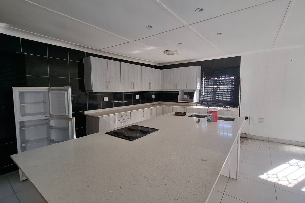 Spacious kitchen featuring a large central island with an integrated electric hob, ample cabinetry, and a modern tiled backsplash.