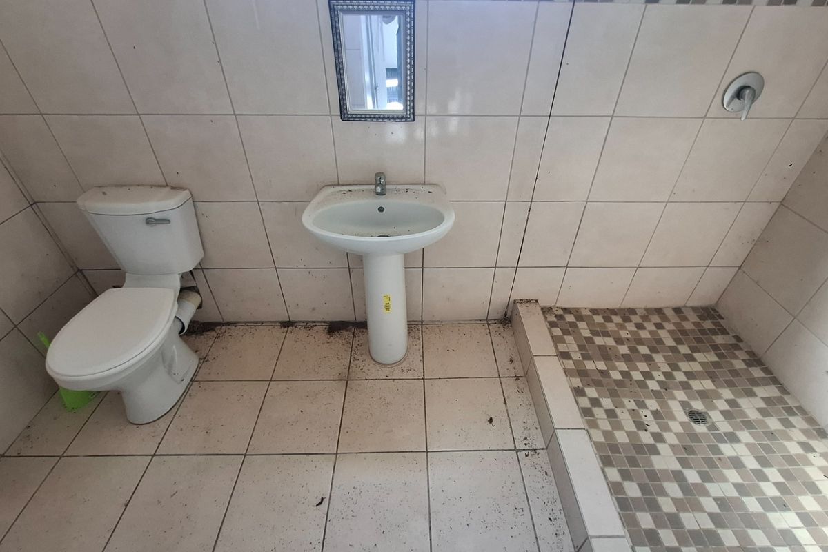 A functional bathroom featuring a pedestal basin, toilet, and shower area with tiled finishes, currently requiring deep cleaning and maintenance.