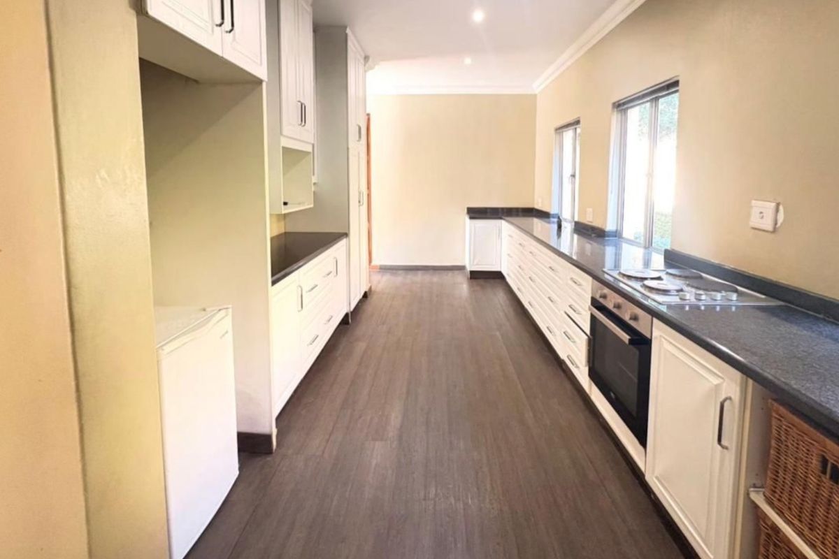 A clean, galley-style kitchen featuring white cabinetry, dark stone countertops, integrated oven and hob, and modern laminate flooring.