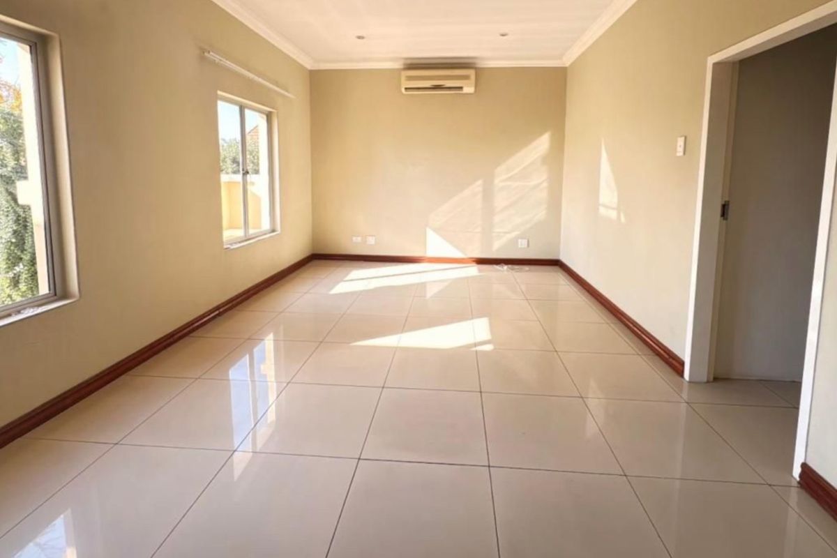 A bright, empty living room featuring neutral tiled flooring, coved ceilings, recessed lighting, and a wall-mounted air conditioning unit.