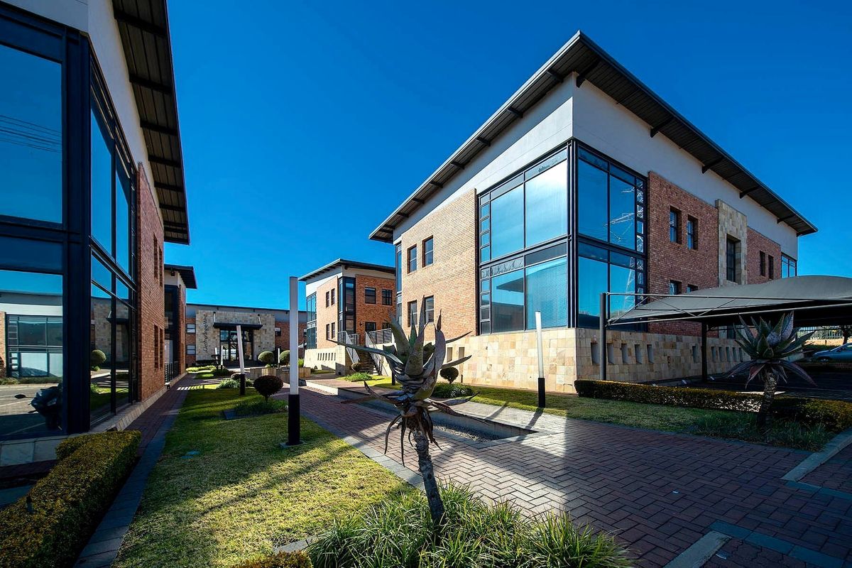 A modern commercial office complex featuring brick and glass facades, well-maintained paved walkways, landscaped gardens, and covered parking facilities.