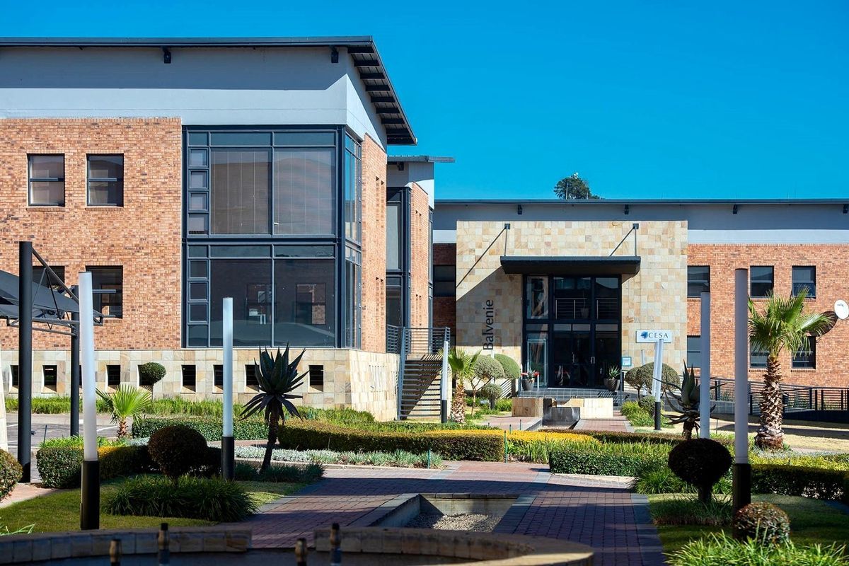A professional exterior view of a modern commercial office building featuring face brick and stone cladding, large glass windows, and a well-maintained landscaped entrance.