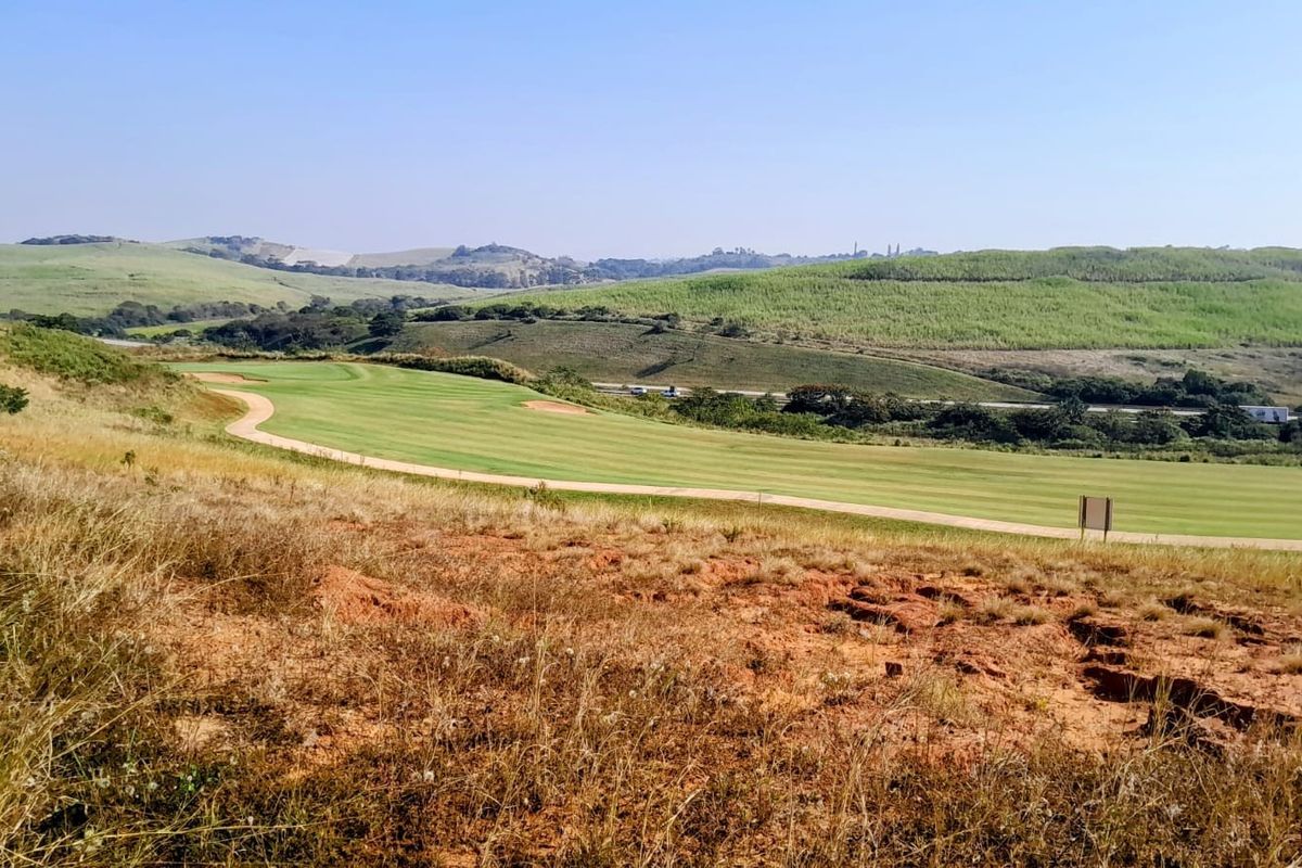 A scenic view overlooking a manicured golf course fairway set against a backdrop of rolling green hills and open landscape.