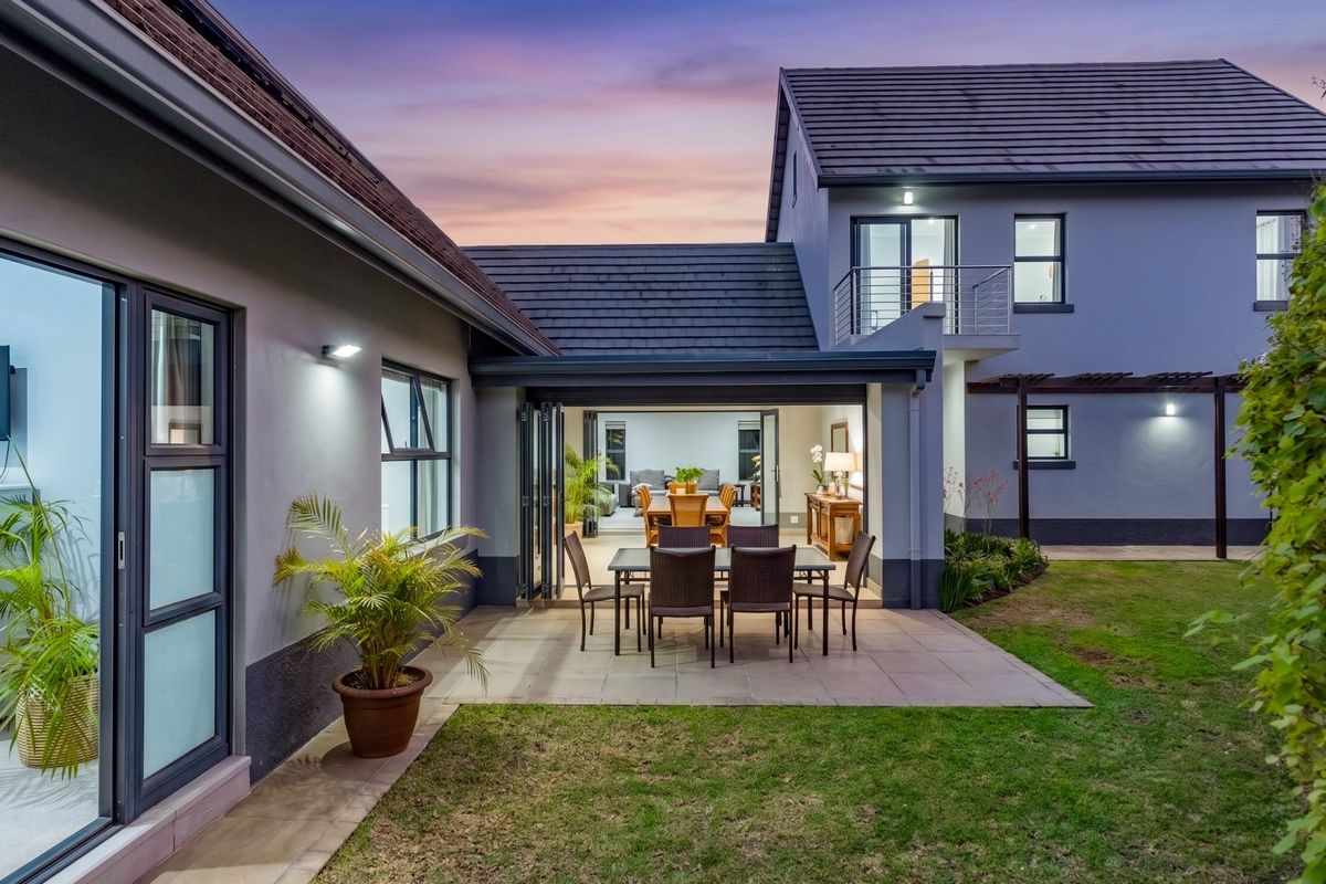 A well-maintained rear exterior view of the townhouse featuring a paved patio, bi-fold doors leading to the interior, and a private garden area.