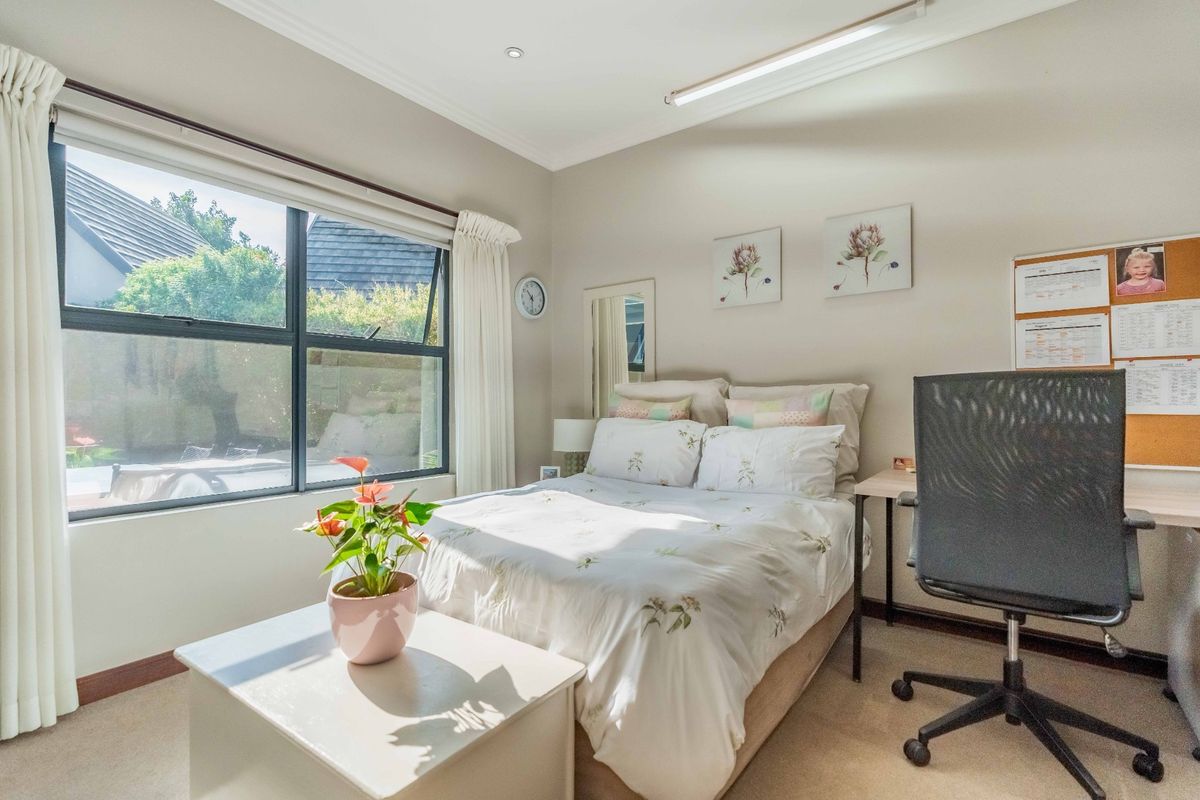 A well-lit bedroom featuring neutral wall tones, carpeted flooring, and a large window providing natural light and garden views.
