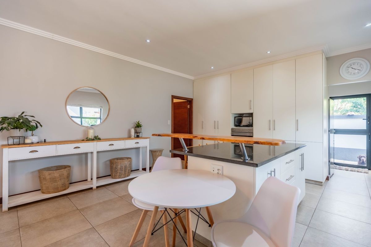 Modern kitchen featuring sleek white cabinetry, granite countertops with a breakfast bar, built-in oven and microwave, and neutral tiled flooring.