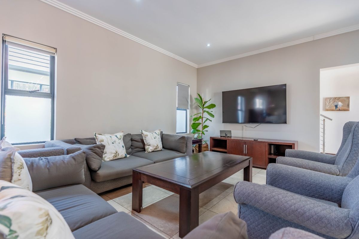 A well-maintained living room featuring neutral wall tones, tiled flooring, recessed downlighting, and coved cornicing, providing a comfortable and functional space.