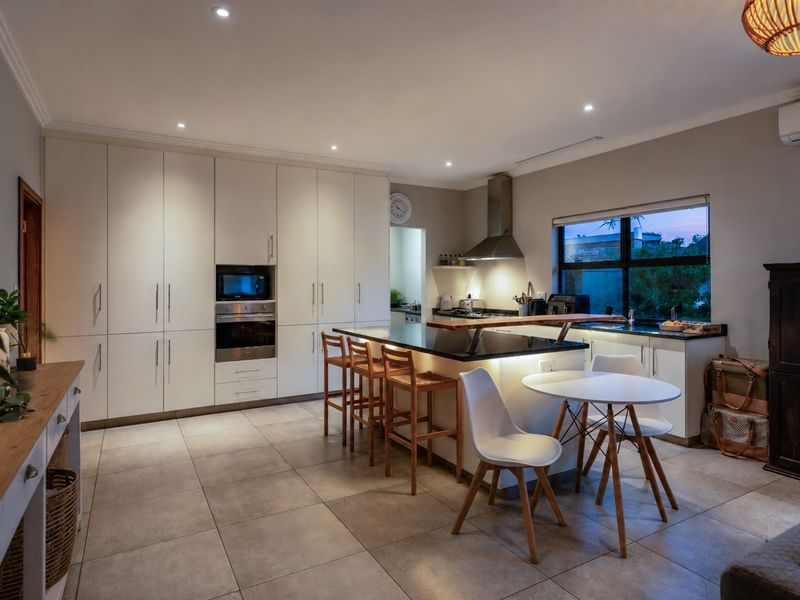 Modern open-plan kitchen featuring sleek white cabinetry, a central island with stone countertops, built-in appliances, and recessed lighting, seamlessly integrated with the living area.