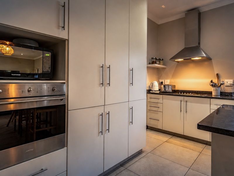 Modern kitchen featuring sleek built-in cabinetry, stone countertops, integrated oven and microwave, and a stainless steel extractor fan with tiled flooring.