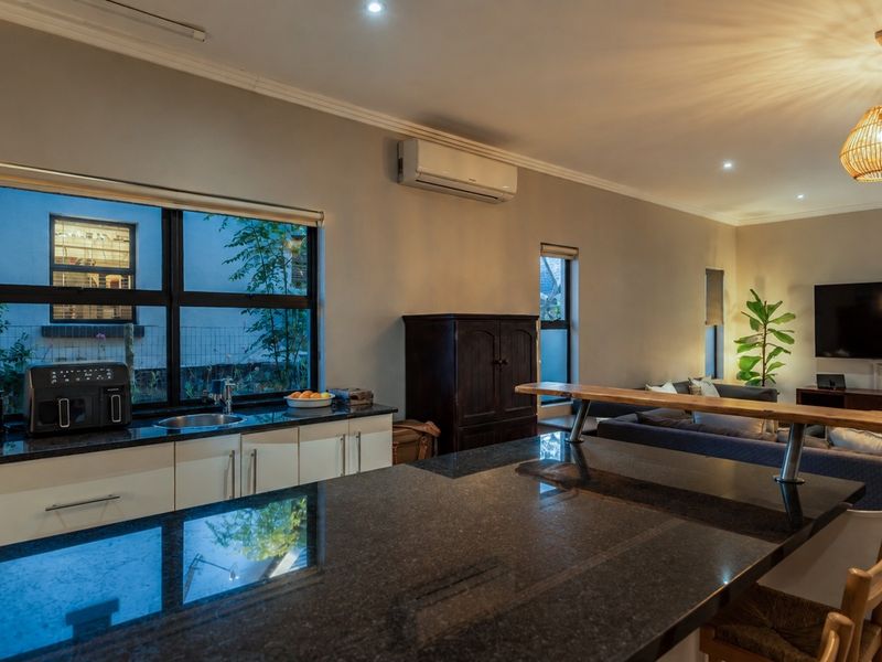 Spacious open-plan living area featuring a modern kitchen with granite countertops, a central island, and integrated air conditioning, flowing into the lounge.
