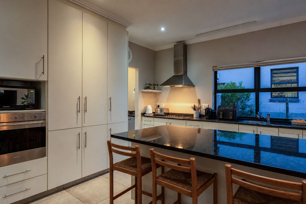 Modern kitchen featuring sleek built-in cabinetry, a large granite-topped island, stainless steel appliances, and tiled flooring with ample storage space.