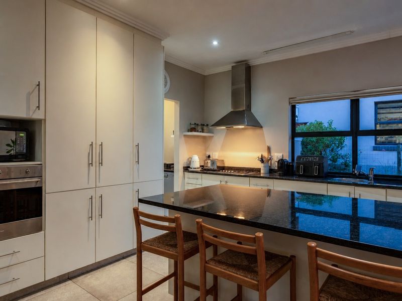 Modern kitchen featuring sleek built-in cabinetry, a large granite-topped island, stainless steel appliances, and tiled flooring with ample storage space.