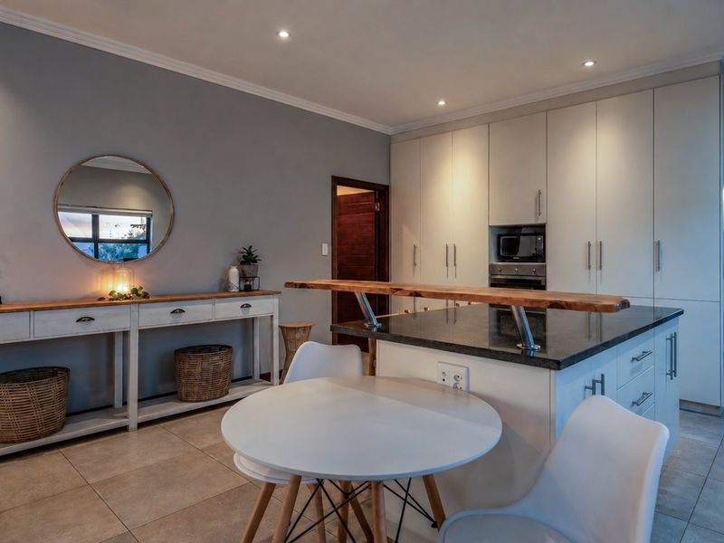 Modern open-plan kitchen featuring sleek white cabinetry, a stone-topped island with a breakfast bar, and neutral tiled flooring, creating a functional and inviting space.