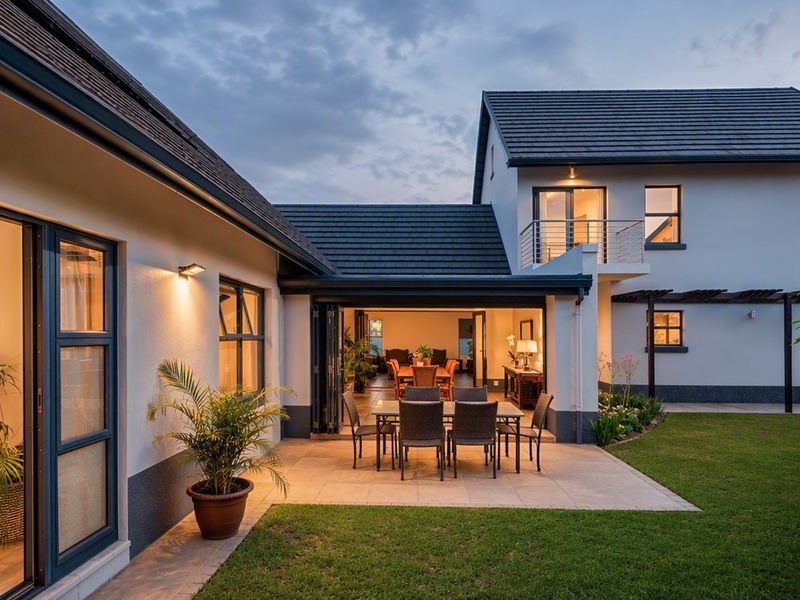 A well-maintained rear exterior view of a townhouse featuring a paved patio, bi-fold doors leading to the interior, and a private garden.