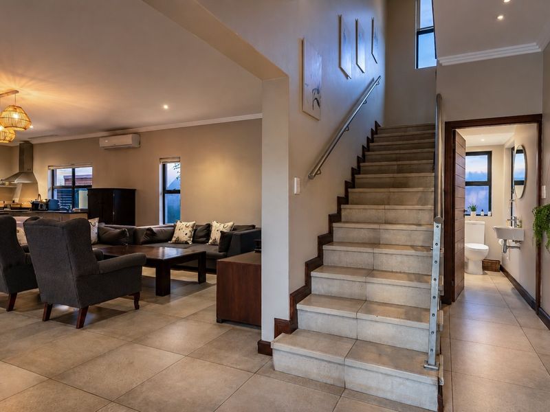 Open plan living area featuring tiled floors, a central staircase with stainless steel handrail, and an adjacent guest bathroom and kitchen.