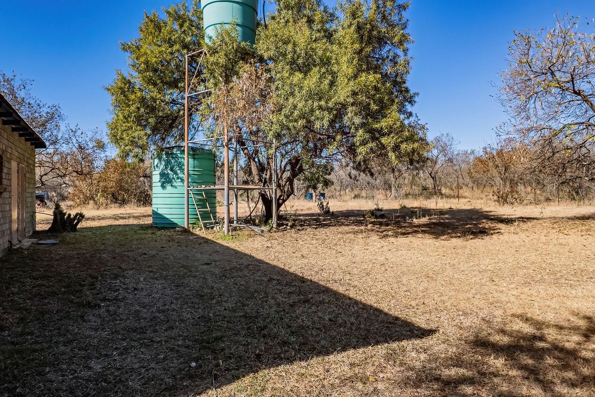 Rear exterior view of the farm property featuring a metal water tank stand and brick wall structure set within a dry landscape.