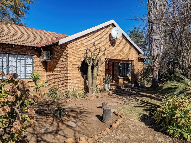 Front elevation of a face brick farm-style house featuring a tiled roof, security bars, and established garden surroundings.