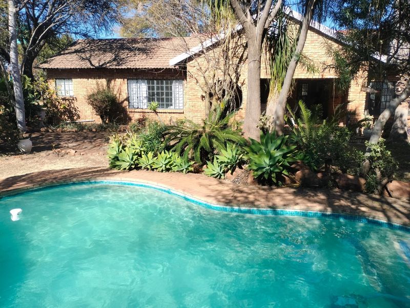 A view of the swimming pool area featuring a brick-built farmhouse exterior with mature garden landscaping and paved surrounds.