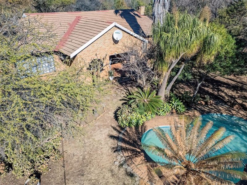 Aerial view of a brick farmhouse featuring a tiled roof, chimney, and a swimming pool set within a mature, tree-lined garden.