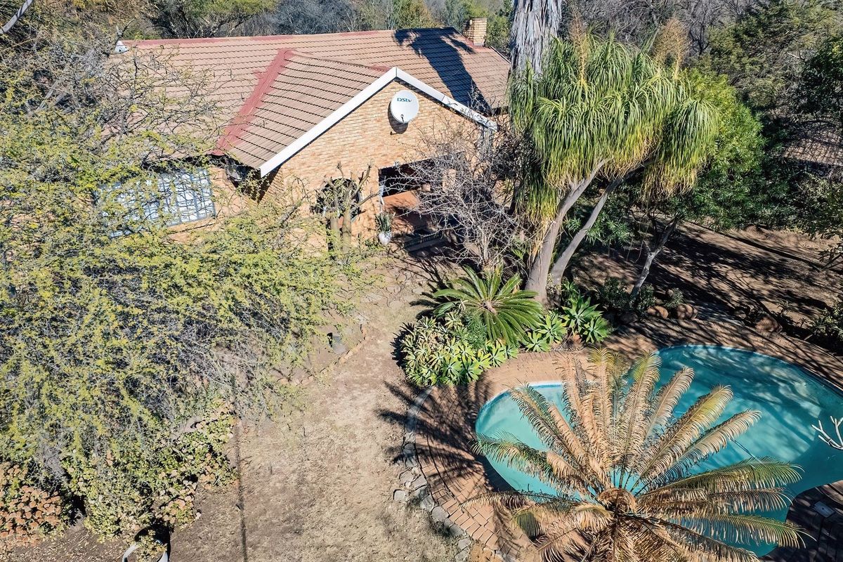 Aerial view of a brick farmhouse featuring a tiled roof, chimney, and a swimming pool set within a mature, tree-lined garden.