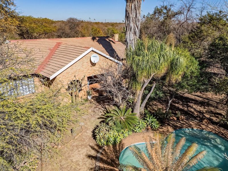 Aerial view of a brick farmhouse featuring a tiled roof, established garden surroundings, and a swimming pool.