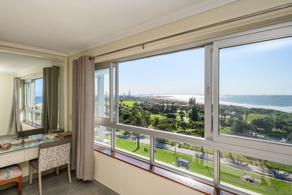 A bedroom featuring large sliding windows that offer expansive views of the coastline, parkland, and ocean.