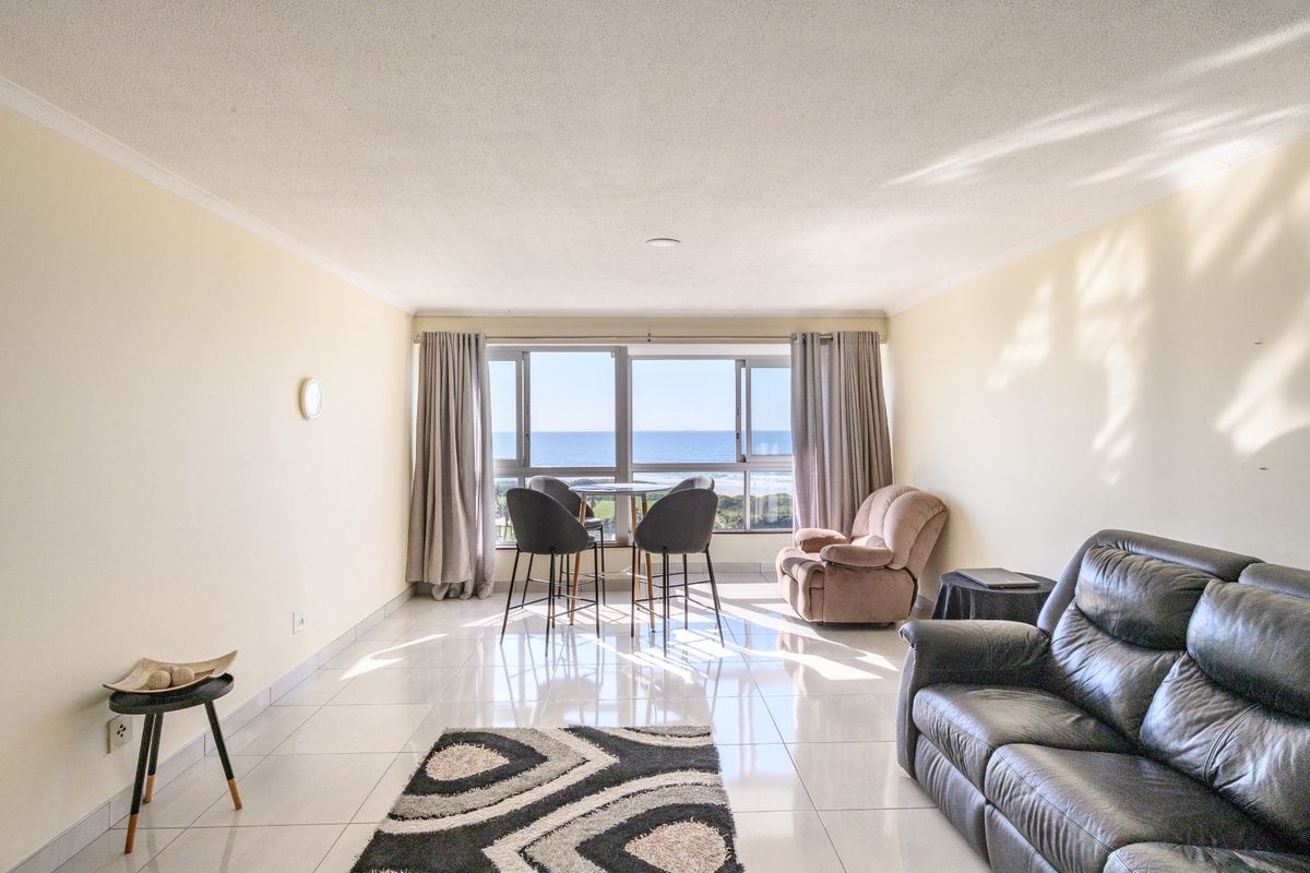 Spacious living area featuring large sliding windows with ocean views, neutral tiled flooring, and a bright, open layout.
