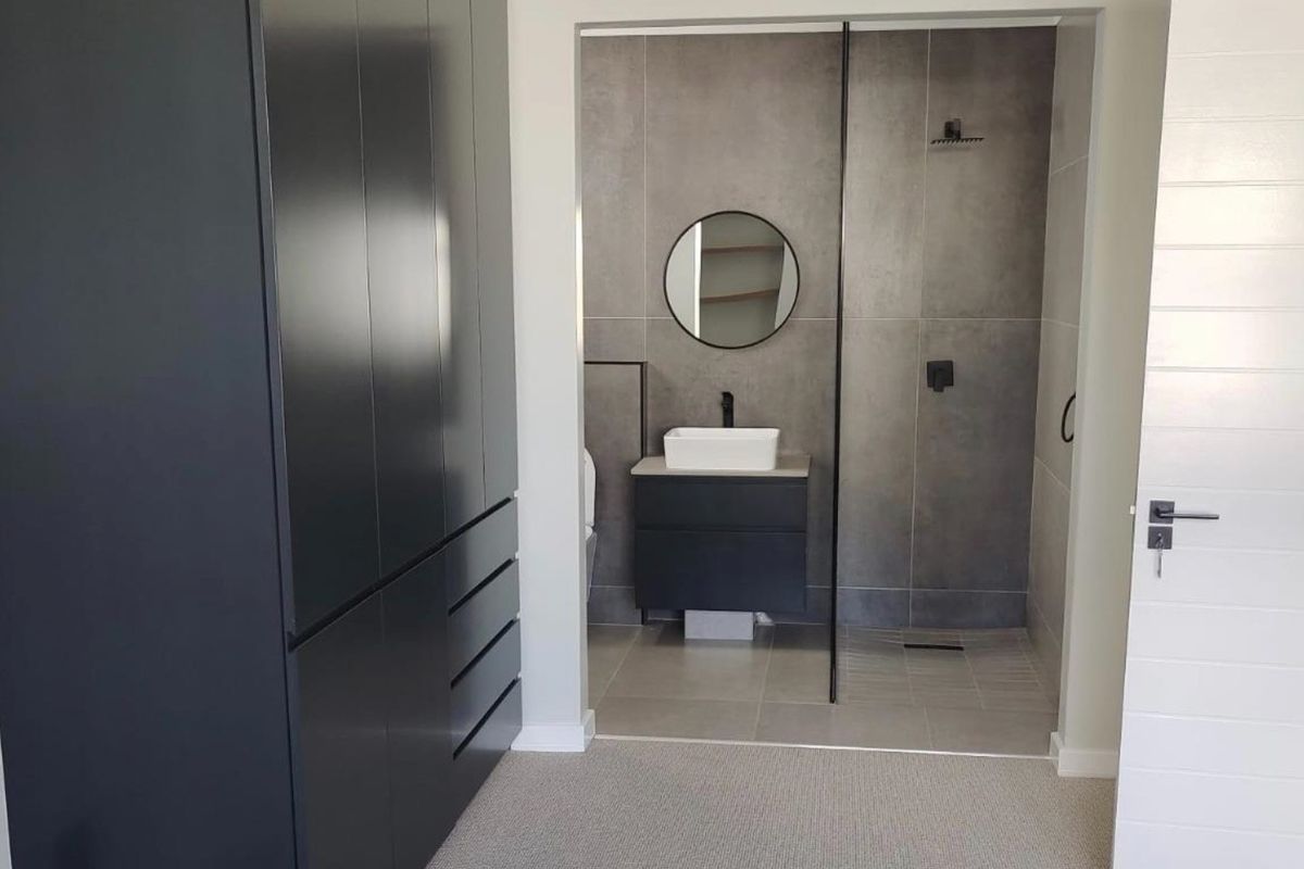 Modern bedroom featuring a large built-in wardrobe and an open-plan en-suite bathroom with a walk-in shower and contemporary vanity.
