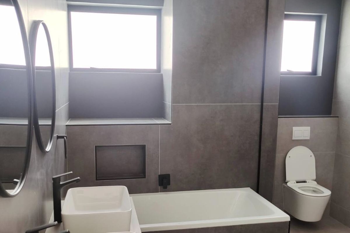 Modern bathroom featuring a double vanity, built-in bathtub, wall-mounted toilet, and sleek matte black fixtures with contemporary grey tiling.