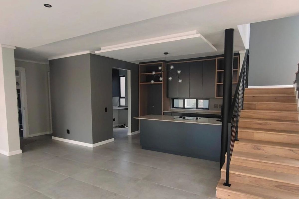 Modern open-plan living area featuring a sleek kitchen island, contemporary cabinetry, and a timber staircase with a black metal balustrade.