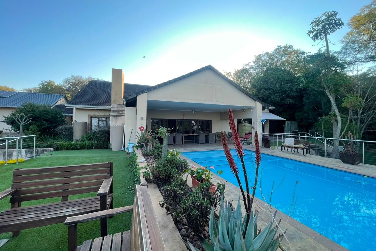 Rear view of the property featuring a covered patio area overlooking a swimming pool and landscaped garden.