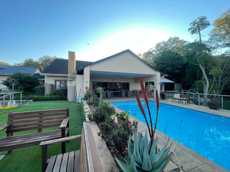 Rear view of the property featuring a covered patio area overlooking a swimming pool and landscaped garden.