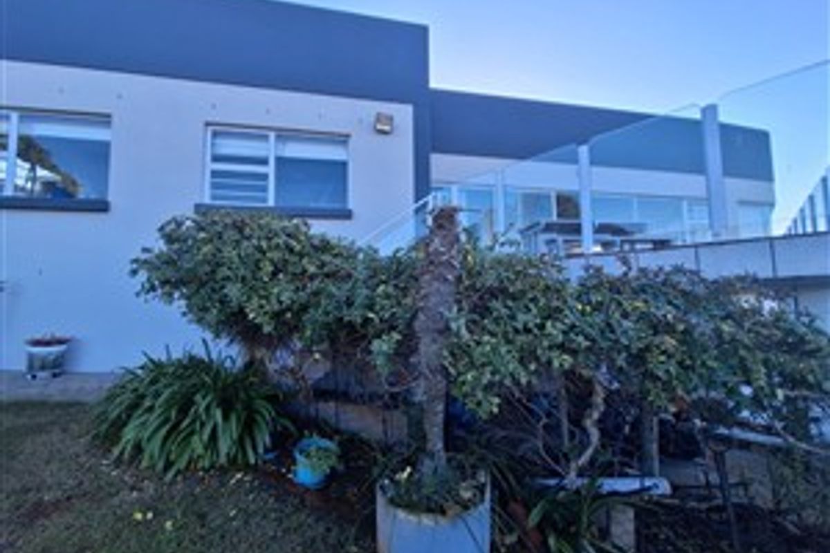 Rear elevation of the property featuring a raised deck with a modern glass balustrade and a paved patio area overlooking the garden.
