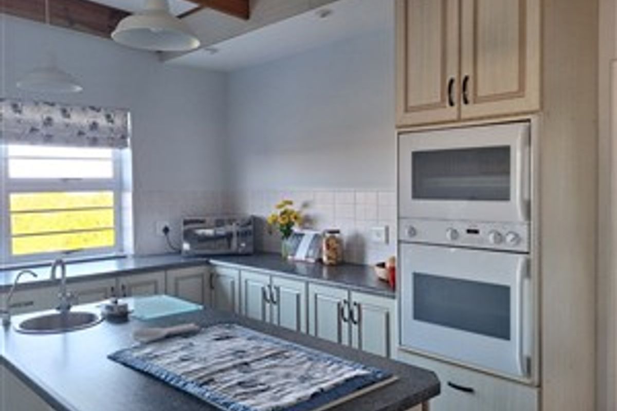 A functional kitchen featuring built-in cabinetry, laminate countertops, a double wall oven, and exposed timber ceiling beams.