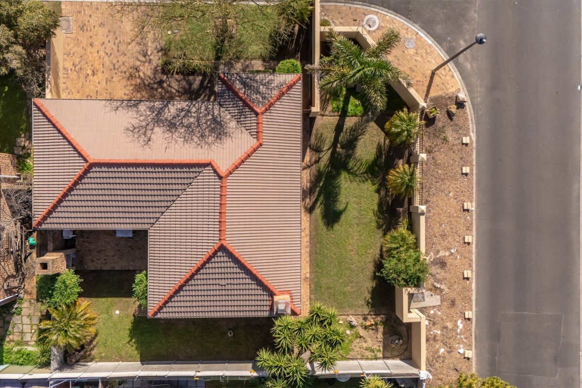Aerial view of the property showcasing the tiled roof structure, paved driveway, and surrounding garden area.