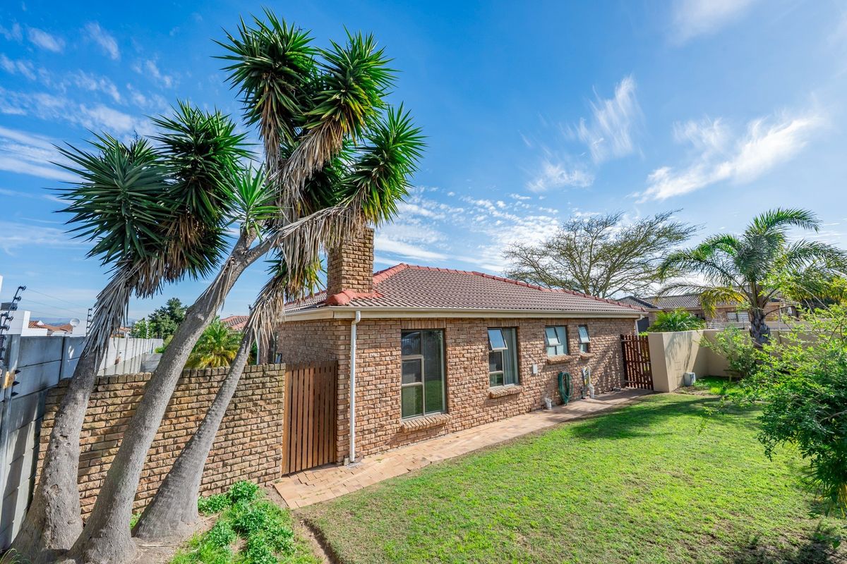 Rear view of a face-brick house featuring a tiled roof, brick chimney, paved walkway, and secure boundary wall with electric fencing.
