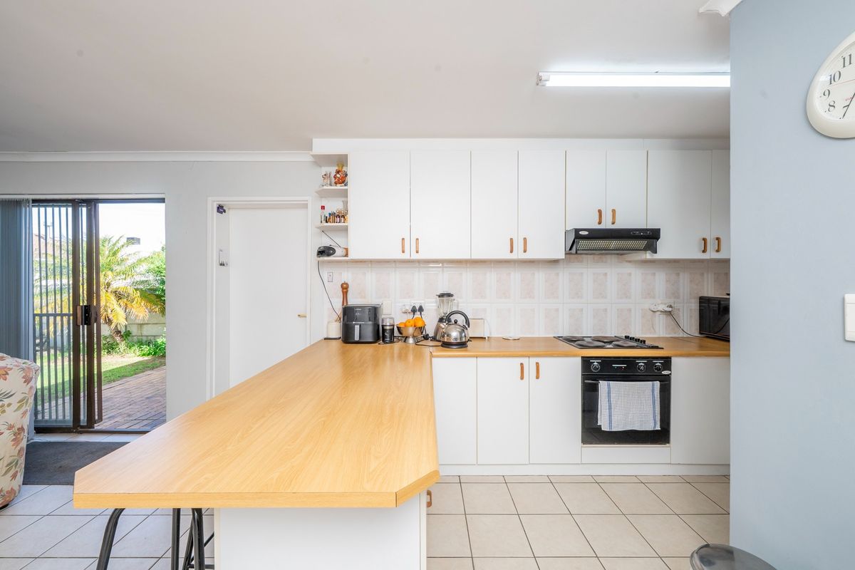 Functional kitchen featuring white cabinetry, wood-look laminate countertops, built-in oven and hob, and direct access to the outdoor patio area.