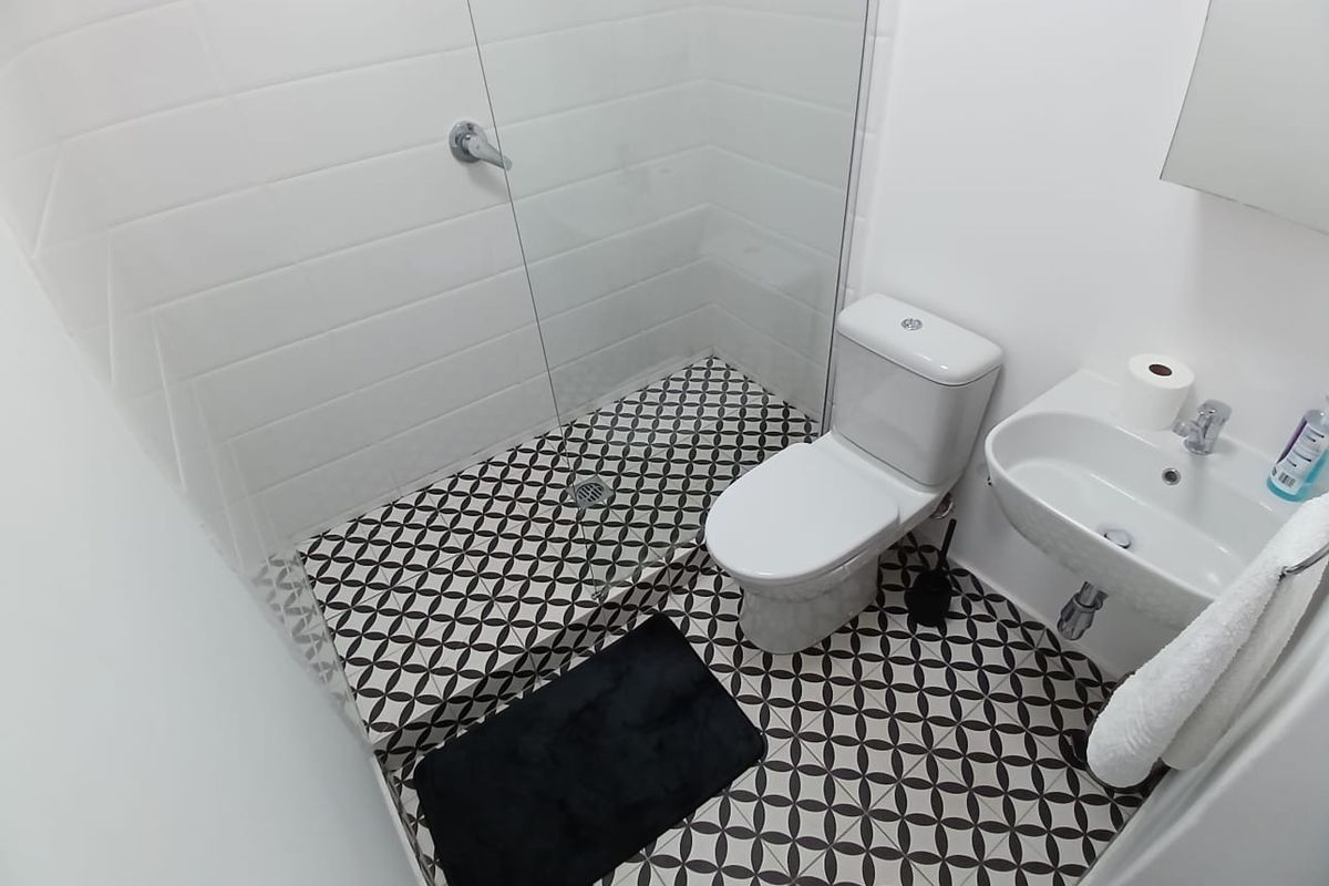 Modern bathroom featuring a walk-in shower with glass screen, patterned floor tiles, white subway wall tiles, and a wall-mounted basin.
